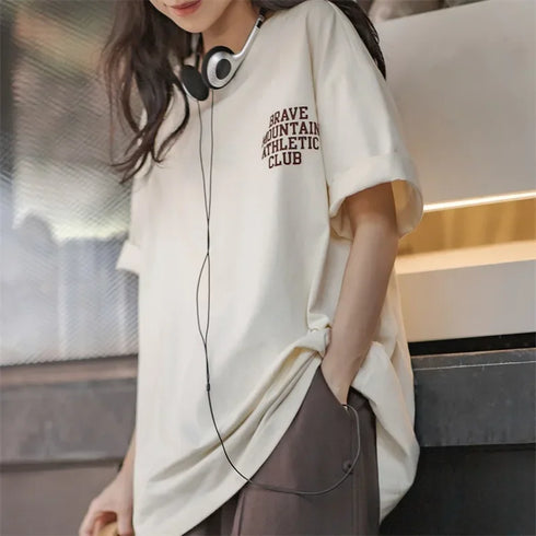 Person wearing a white t-shirt with text and headphones, standing indoors.